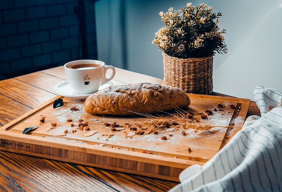 baked bread near cup of coffee both on brown wooden board, bread beside white ceramic teacup on brown wooden board HD wallpaper