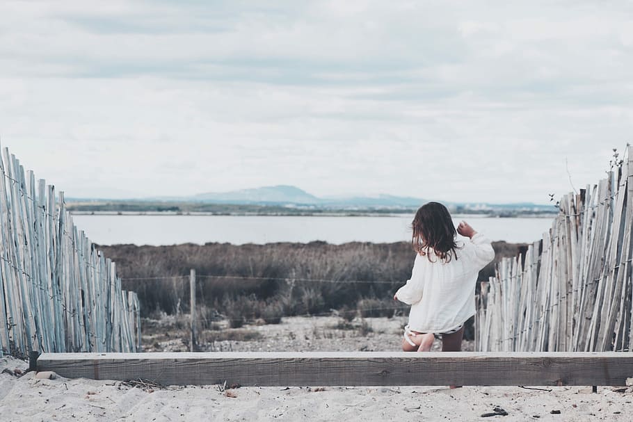 girl stepping down on wooden steps with wooden fence towards brown grassfield, person standing in the middle of fences HD wallpaper