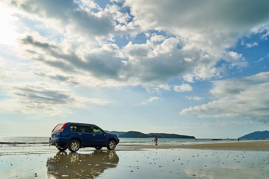 blue SUV near person standing on seashore in distant of mountains HD wallpaper