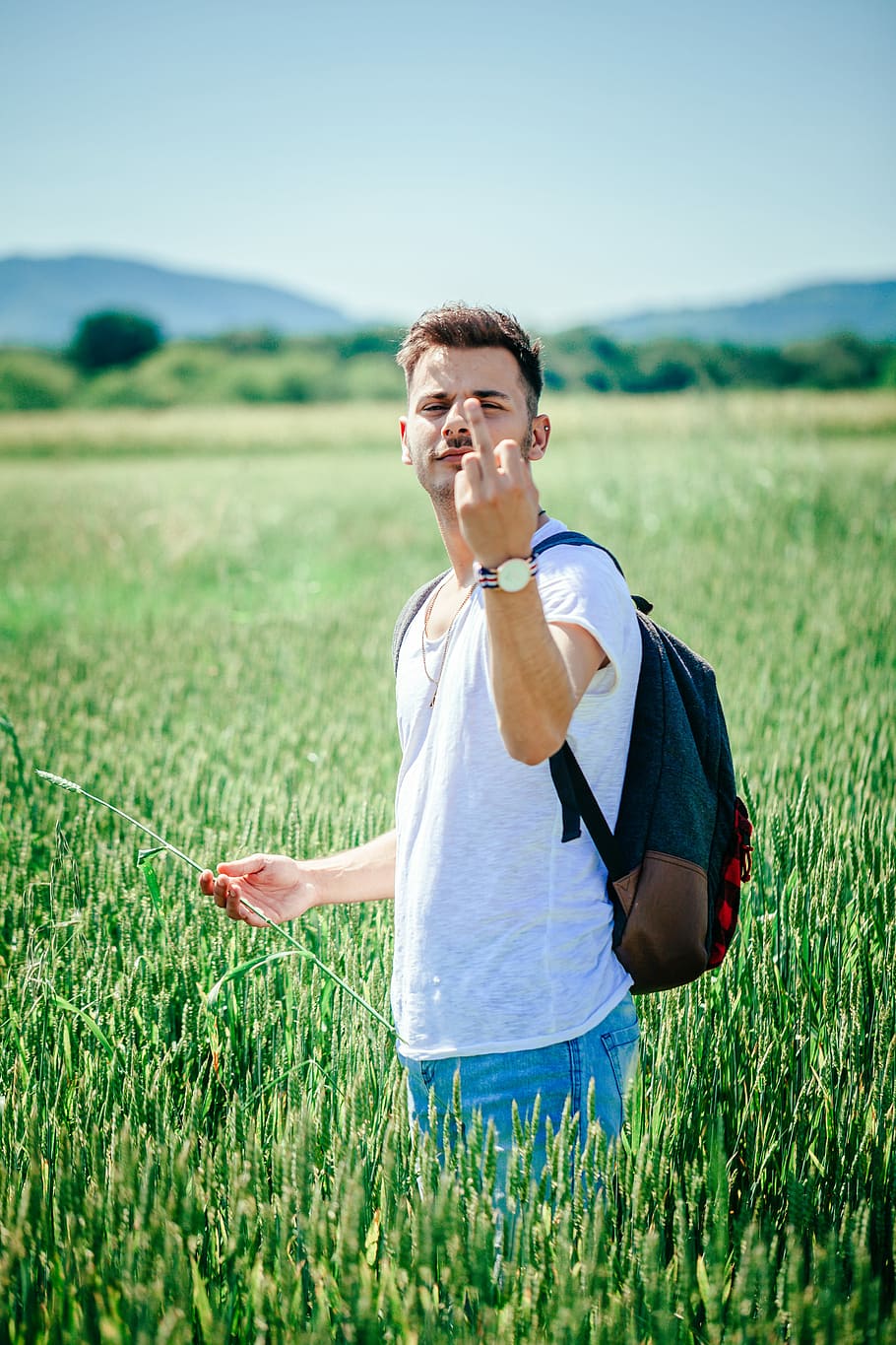man standing on green plant field, man in white shirt showing middle finger during daytime