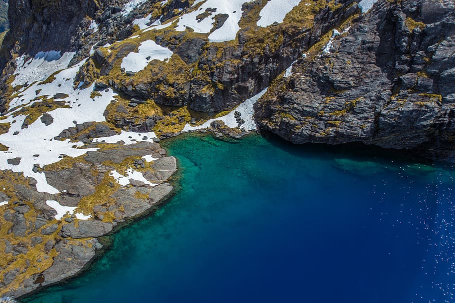 aerial view of body of water near large rocks, gray stone with snow near body of water HD wallpaper