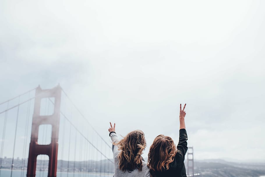 two women raising hands near Golden Gate bridge at daytime, person