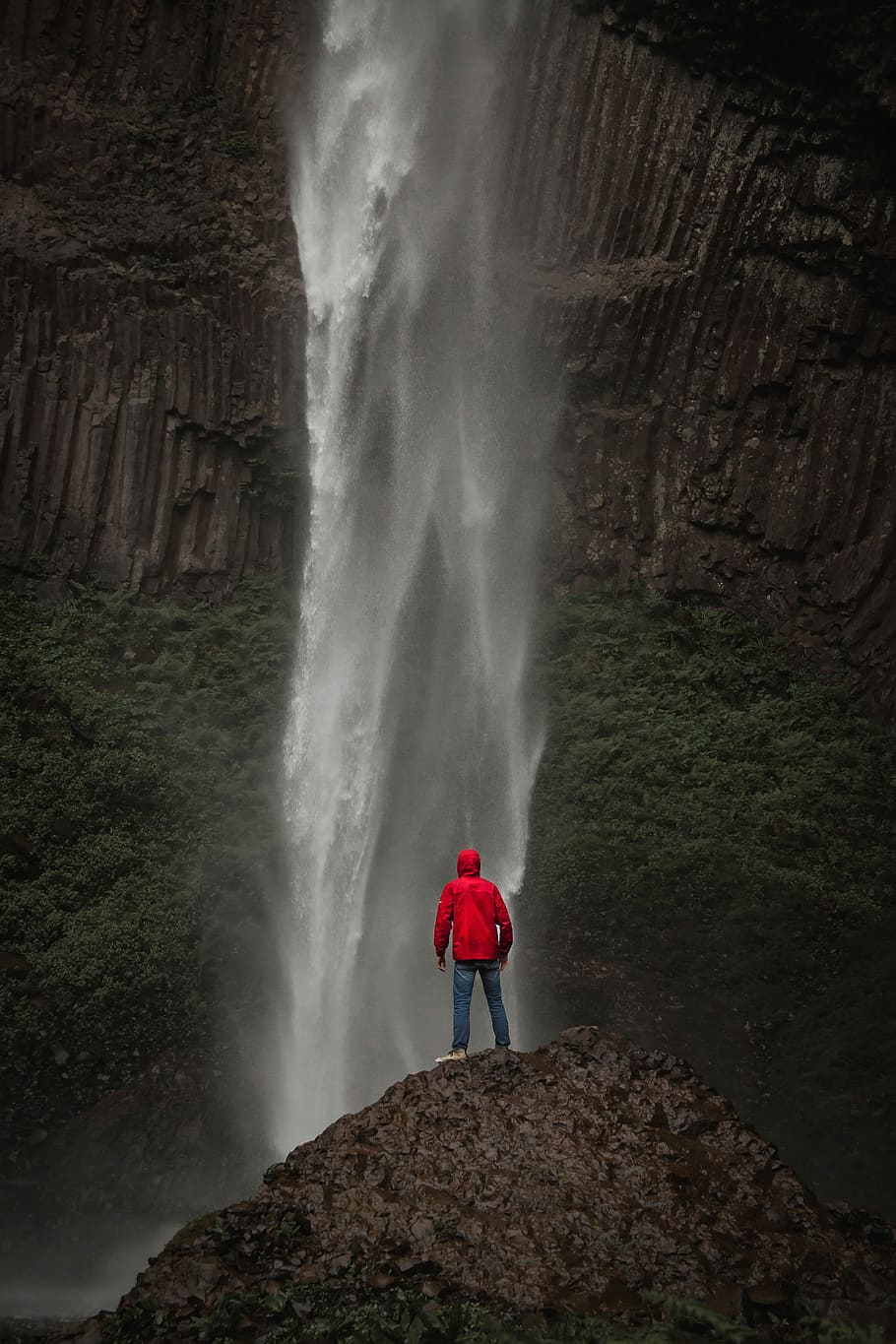 person wearing red jacket and blue denim jeans standing in front of waterfall, man standing on cliff in front of waterfalls during daytime, HD wallpaper