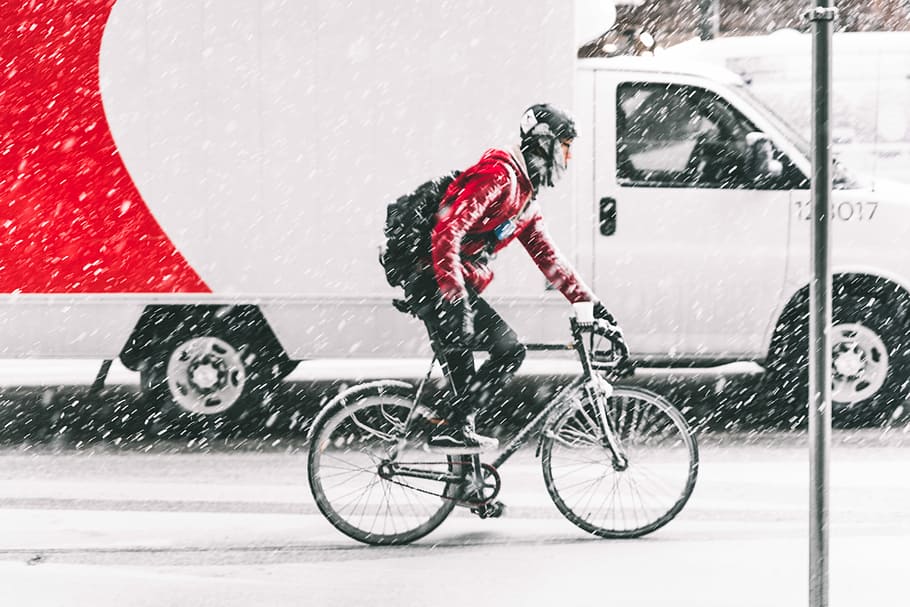 person in red jacket riding on mountain bike with white vehicle nearby during winter, man cycling on snowy weather