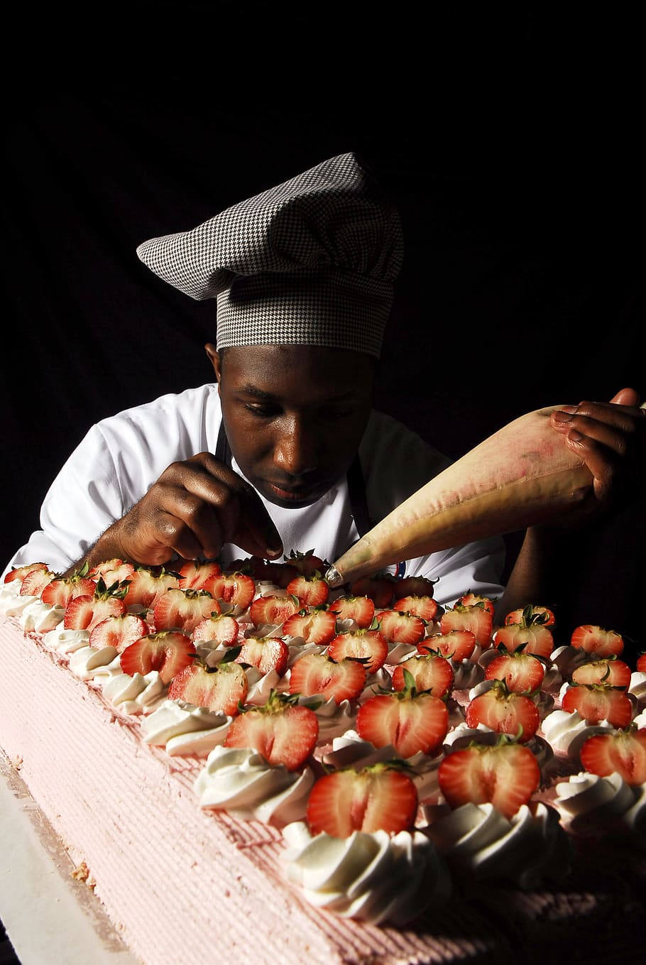man putting icing on cake topped with slices on strawberries HD wallpaper
