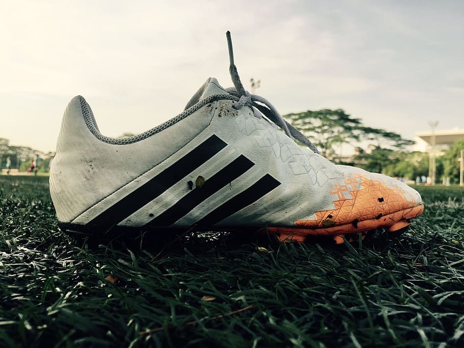 closeup photography of white and orange adidas cleat shoe on green grass