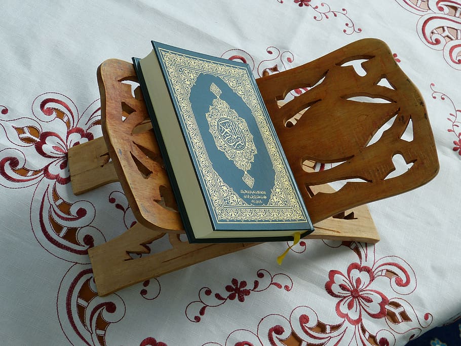 green and gold hardbound book and brown wooden holder, quran