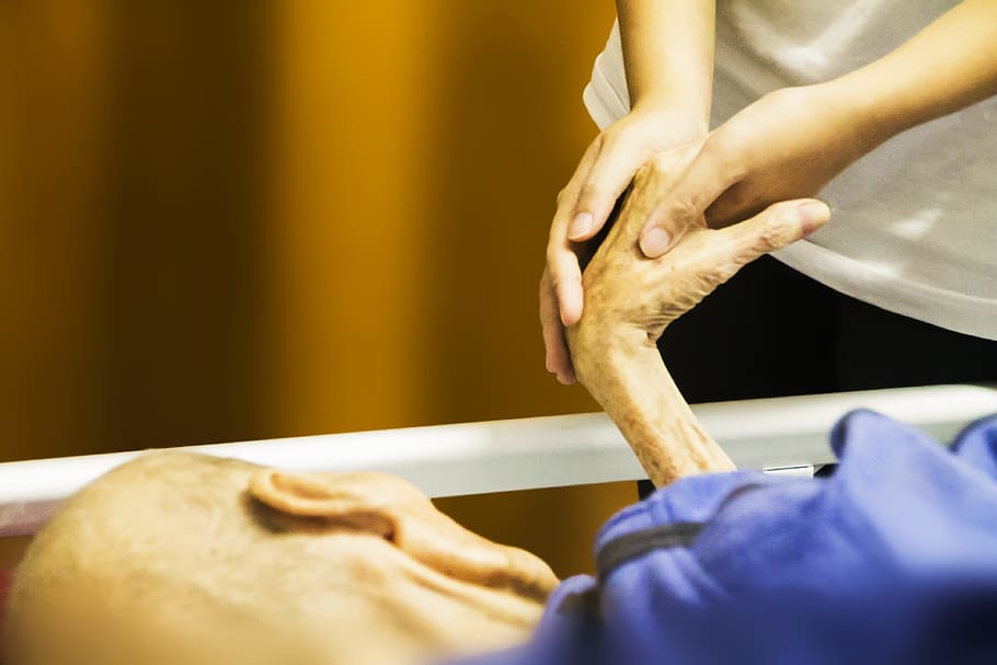 person holding the hand of person lying on bed, hospice, hand in hand