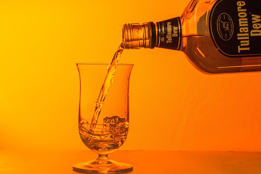 person pouring Tullamore Dew beverage in clear snifter glass HD wallpaper
