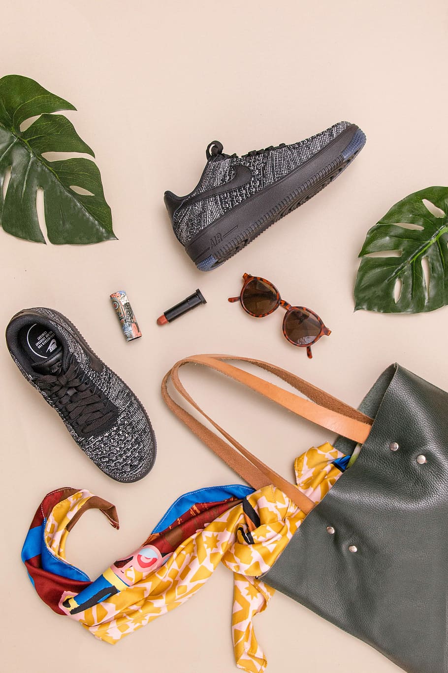 photo of bag, sneakers, and sunglasses on beige surface, pair of gray Nike low-top sneakers beside black leather tote bag