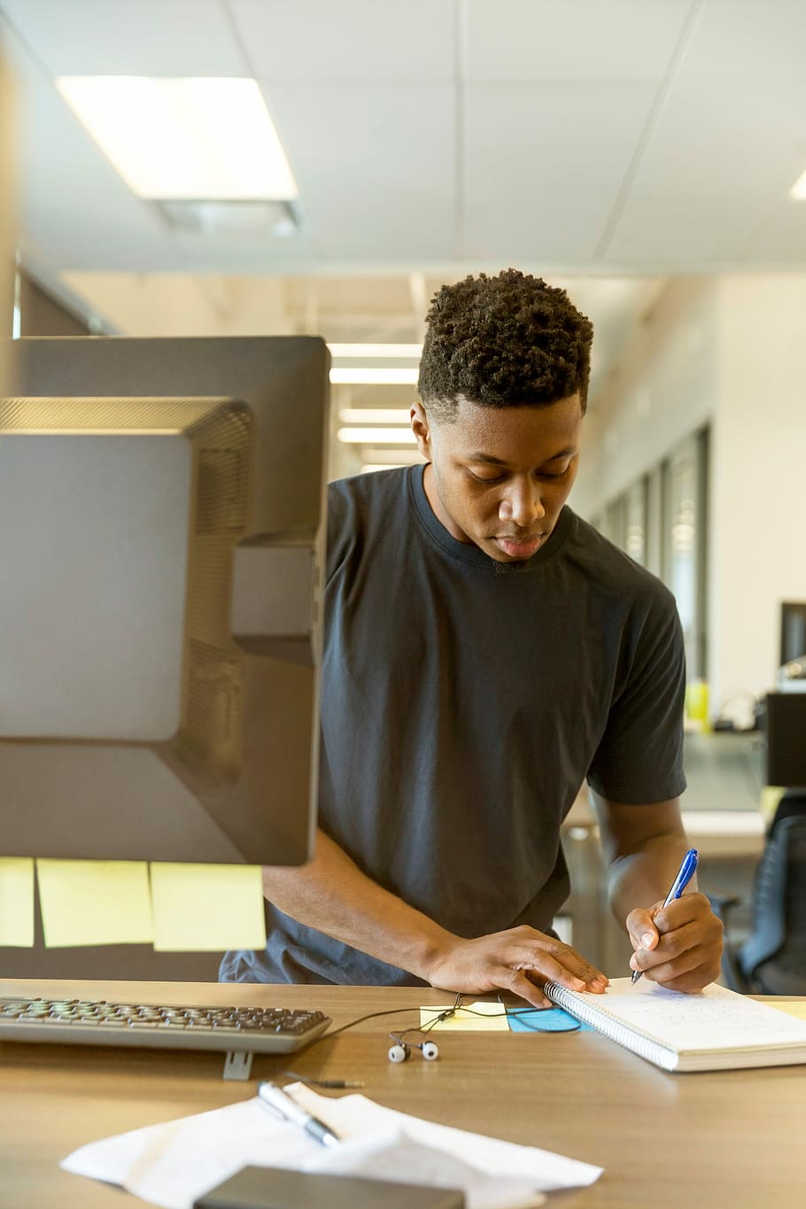 man writing on white paper, man standing in front of computer monitor writing on notebook on brown wooden table HD wallpaper