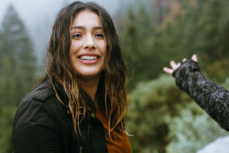 woman wearing black jacket smiling with forest background, woman standing next to trees HD wallpaper