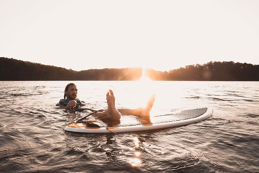 man floating on body of water, man putting his feet on surfboard HD wallpaper