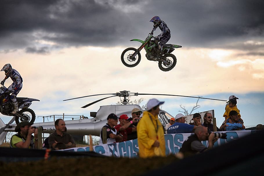 man riding motocross dirt bike over crown of people during daytime, person doing dirt motorcycle trick over helicopter
