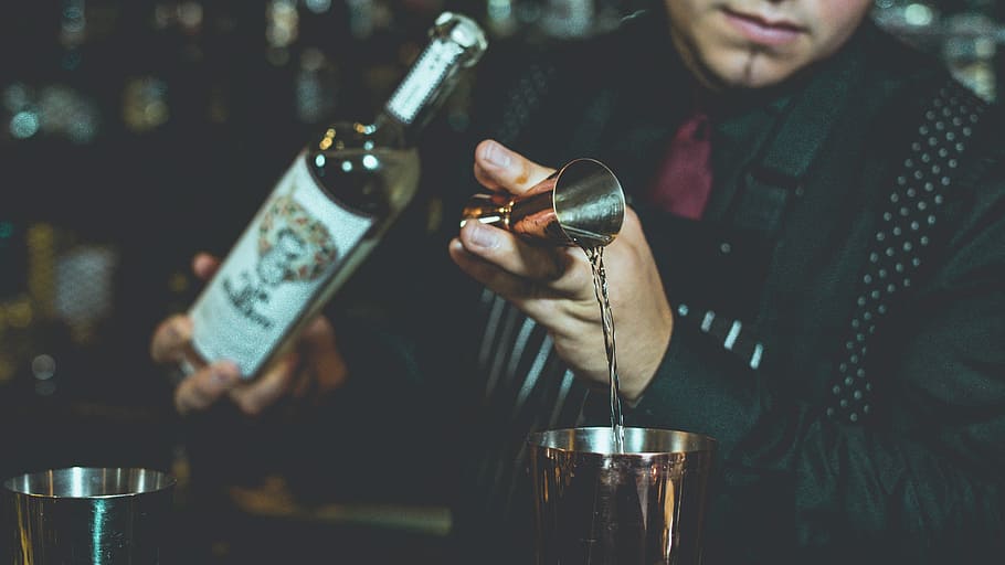 bartender mixing tequila on table, close-up photography of man wearing black suit holding bottle during daytime HD wallpaper
