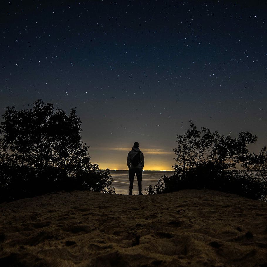 man standing in front of body of water, man staring at the desert under the starry night