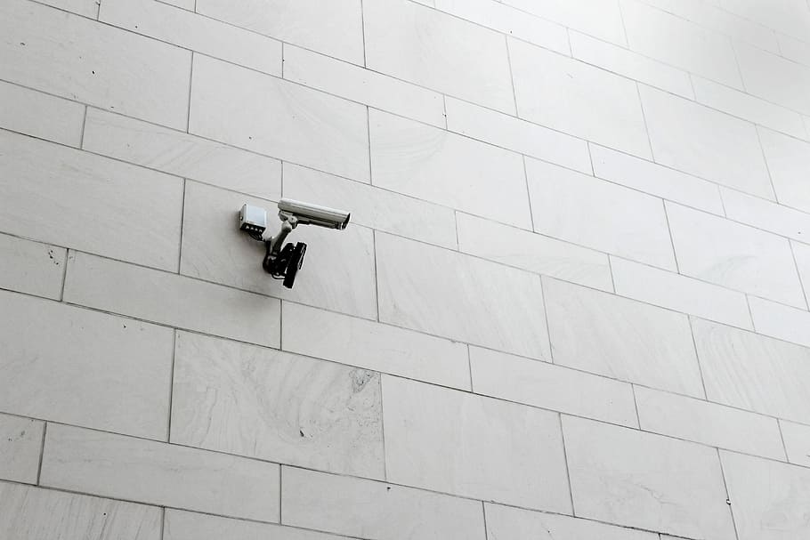 grey surveillance camera on wall, white CCTV camera on white marble wall