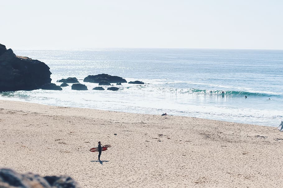 man holding red surfboard on beach, person holding surfboard in seashore during daytime HD wallpaper