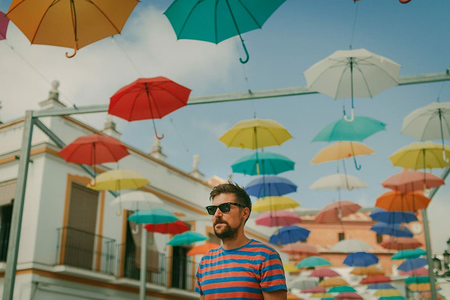 man wearing blue and red striped crew-neck t-shirt and black framed sunglasses, shallow focus photo of man standing near umbrellas, HD wallpaper