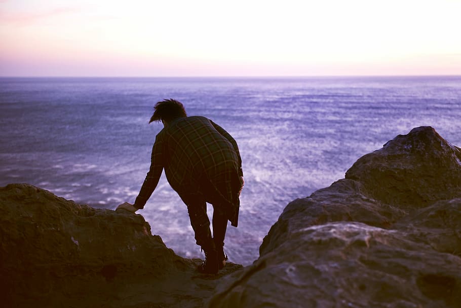 man on top of rock beside body of water, person on edge of cliff HD wallpaper