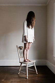 woman in white long-sleeved dress standing on white wooden chair near corner of the room HD wallpaper