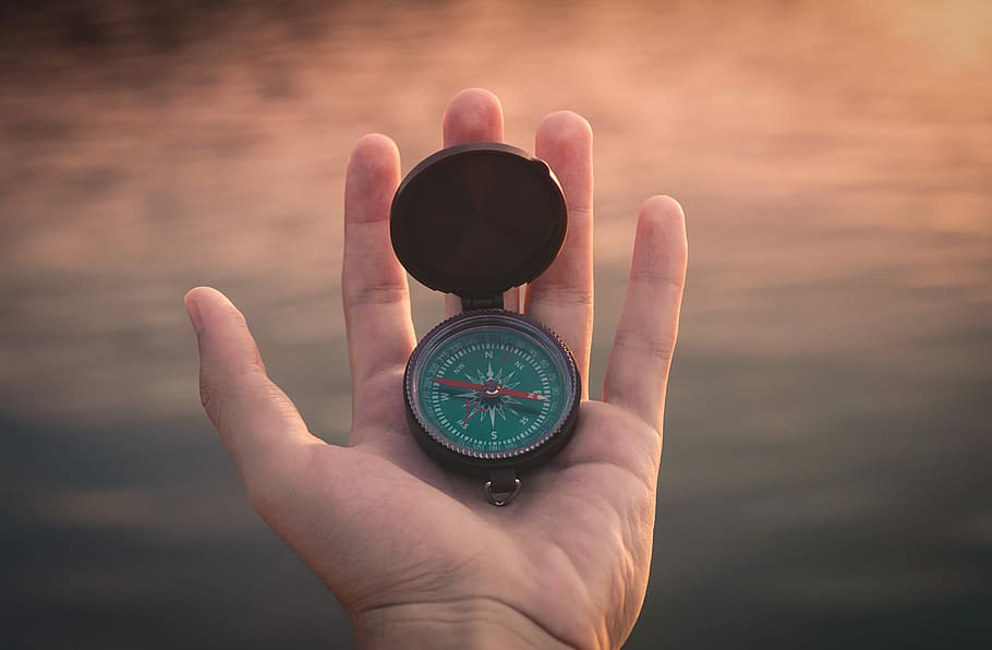 person holding black and green compass pointing to west, person holding brown compass HD wallpaper