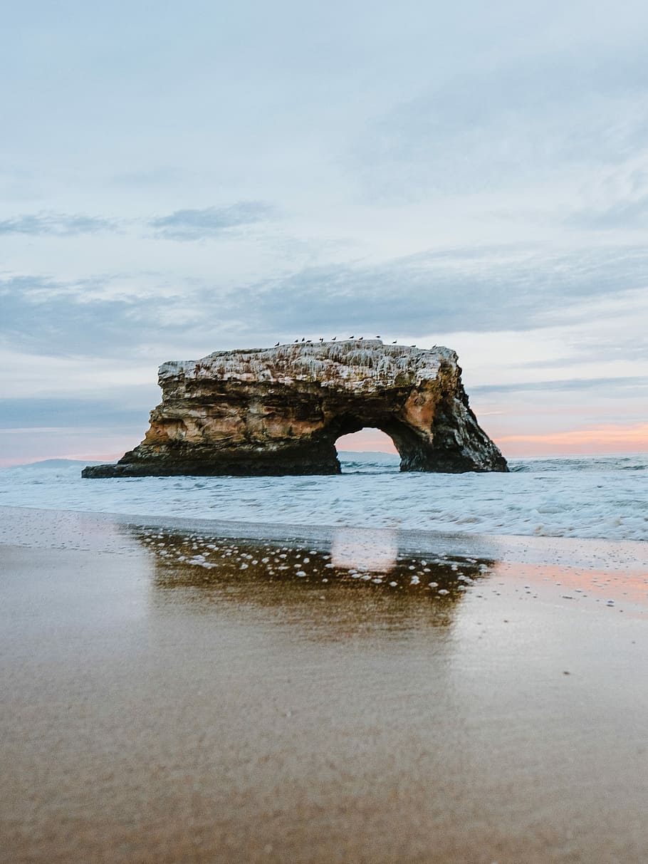 sea stack under the cloudy sky, brown and black rock formation by sea HD wallpaper