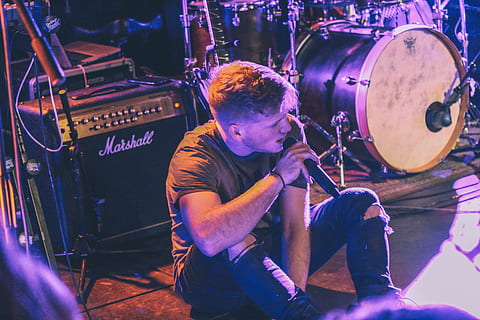 vocalist man holding microphone sitting in front of Marshall guitar amplifier near drum kit, man sitting on stage holding microphone HD wallpaper