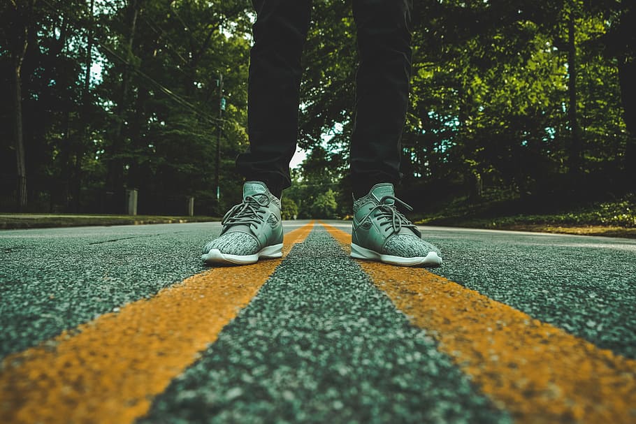 person standing on concrete road, person wearing pair of gray shoes standing on yellow lane road
