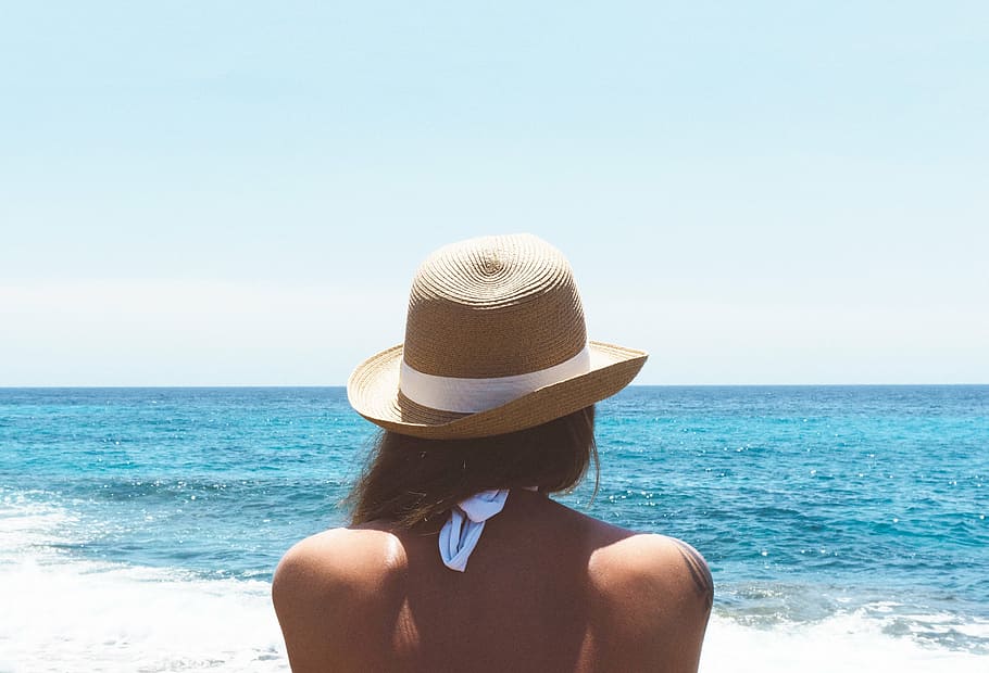 woman in front of body of water wearing brown hat during daytime