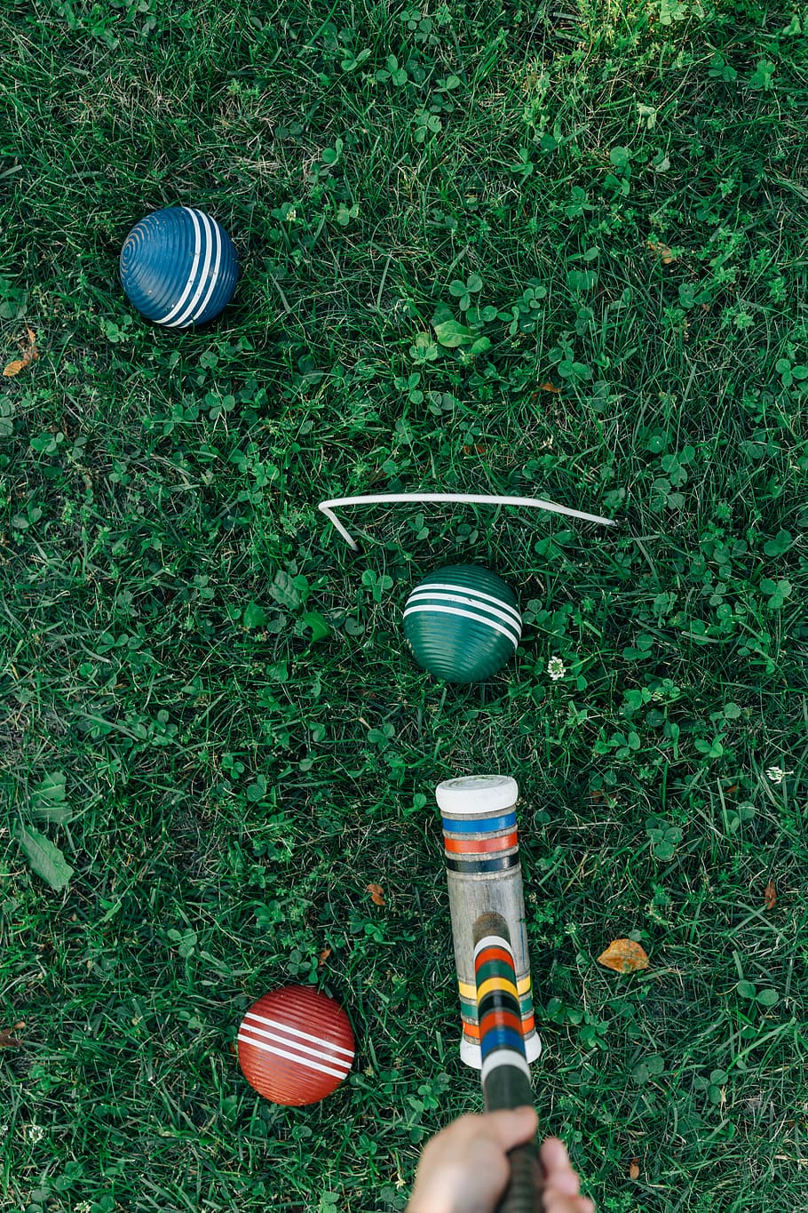 person playing croquet, three cricket balls with bat on green grass