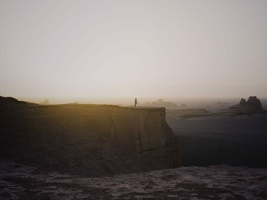 person standing on cliff under white sky, man standing on mountain edge HD wallpaper