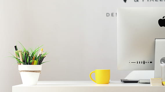yellow ceramic mug beside gray aluminum iMac, yellow cup placed on top of desk near iMac HD wallpaper