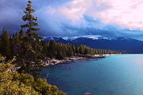 body of water near mountain, green leafed tree besides blue body of water under white cloudy sky during daytime HD wallpaper