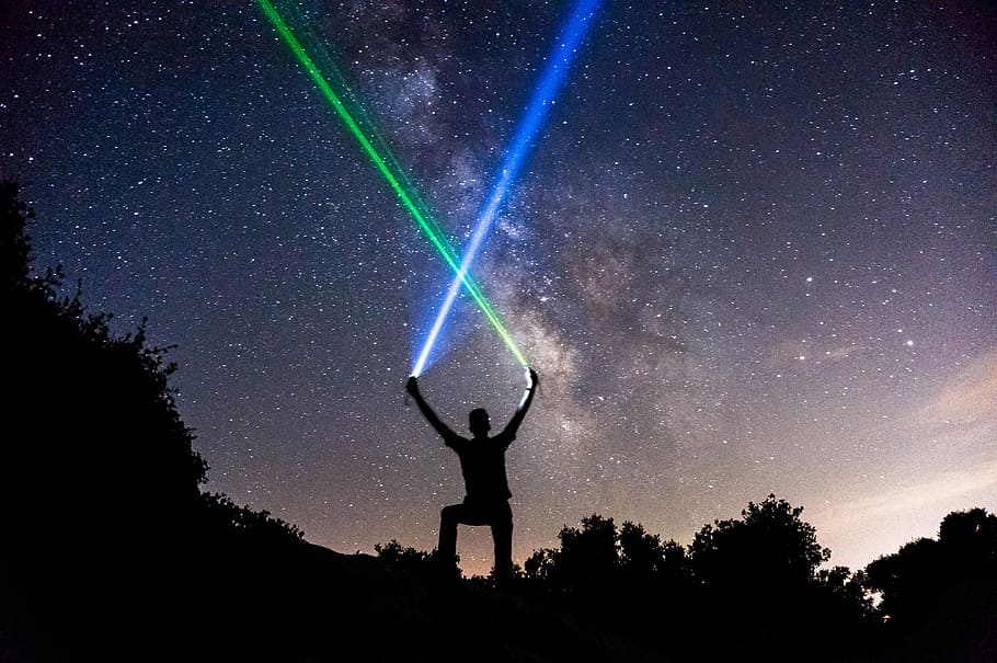 Man wielding blue and green lightsabers in the starry night sky