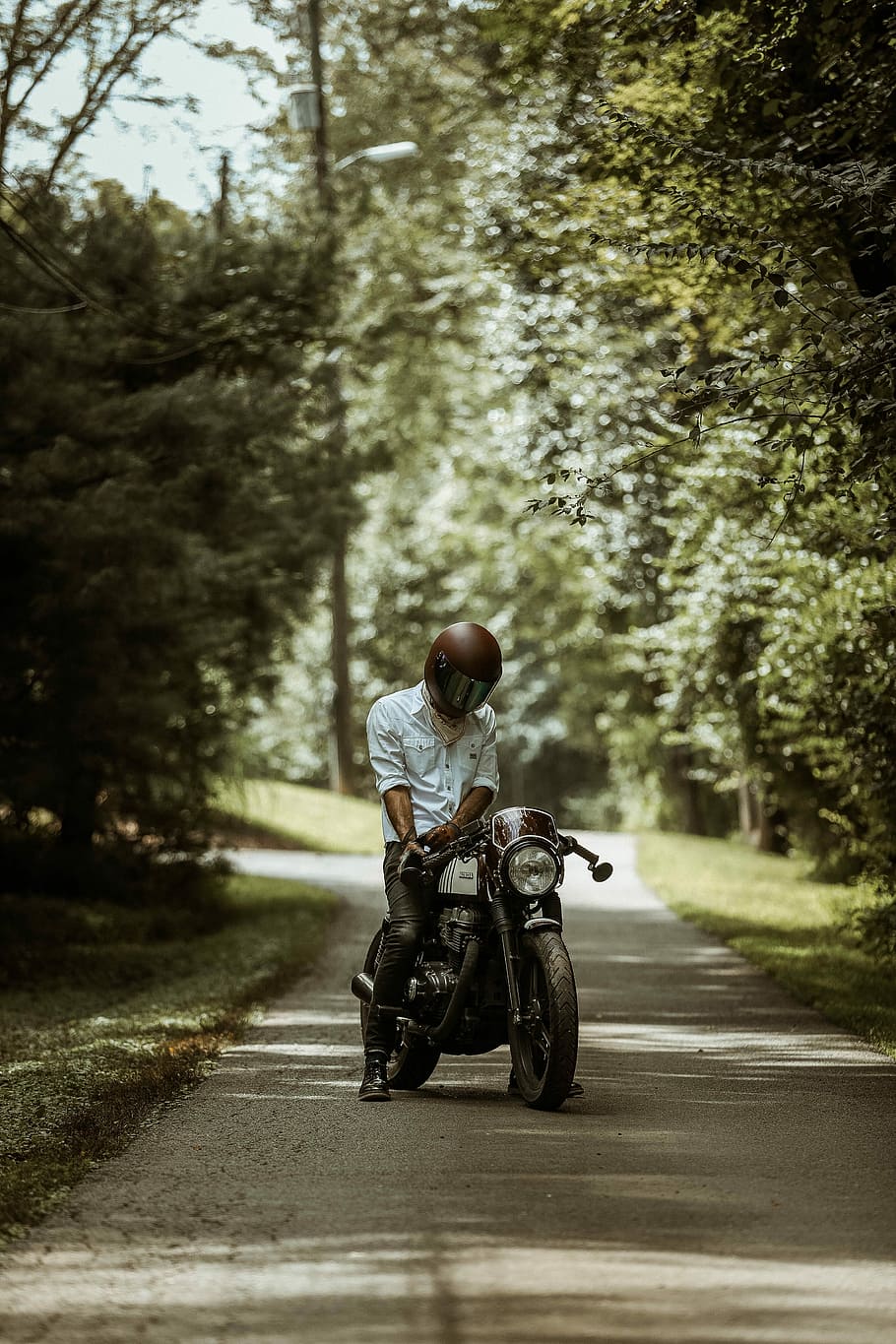 man riding motorcycle on pathway, man wearing full-face helmet while riding motorcycle on asphalt roadway between trees during daytime