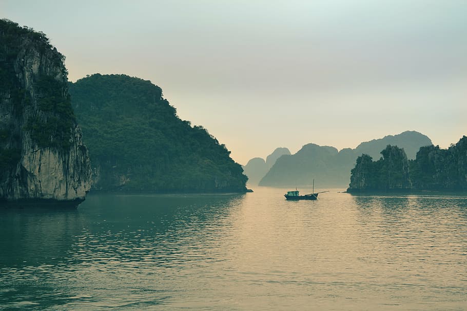 boat on calm body of water near rock formation covered by trees under white sky during daytime HD wallpaper