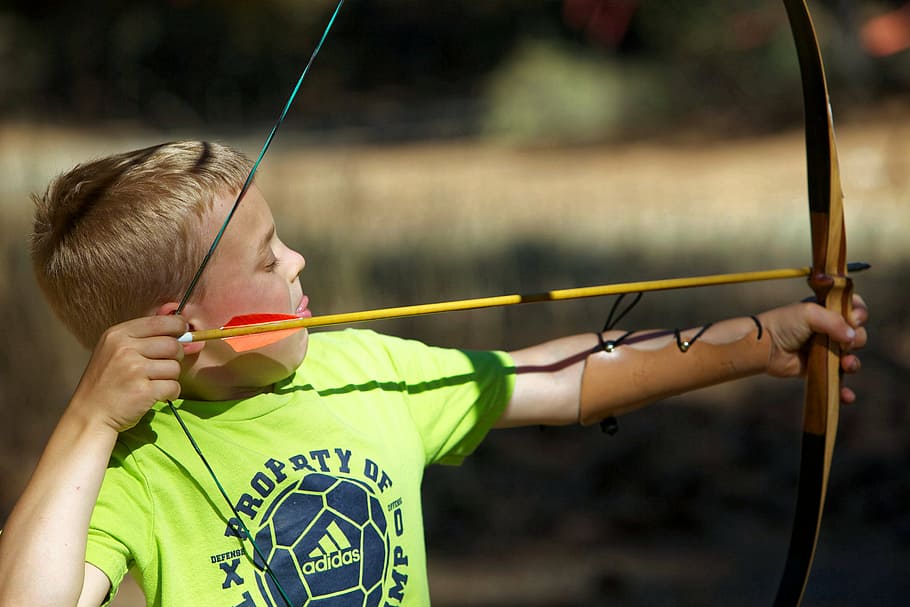 selective focus photography of boy shooting arrow on bow during day HD wallpaper