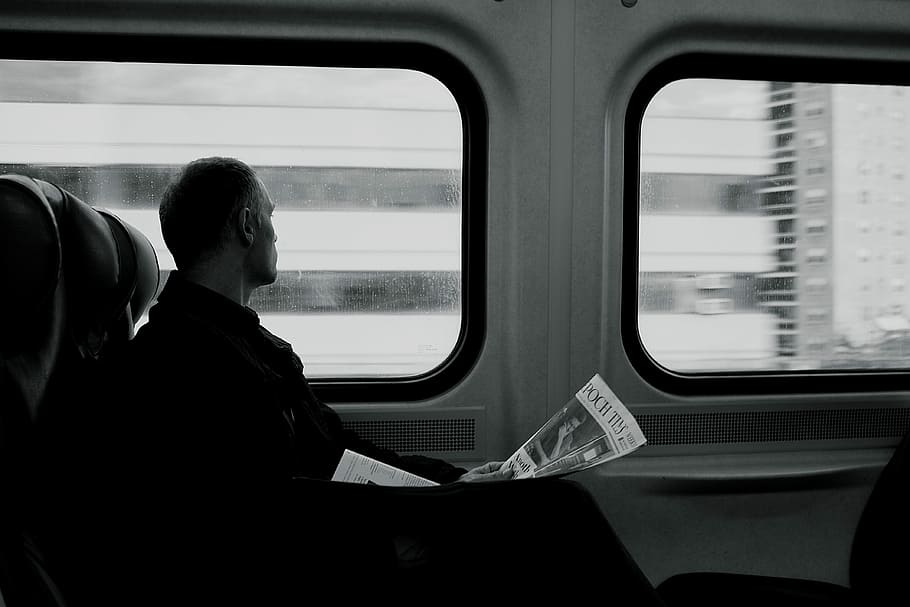 man inside train looking on window while holding newspaper grayscale photography, grayscale photo of a man looking at window