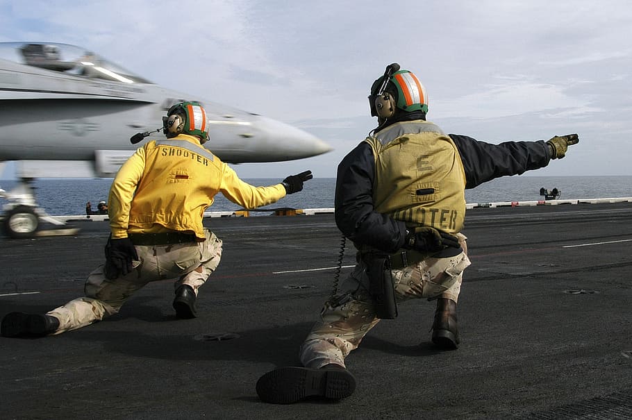 gray fighter jet about to take off, sailors signal to launch