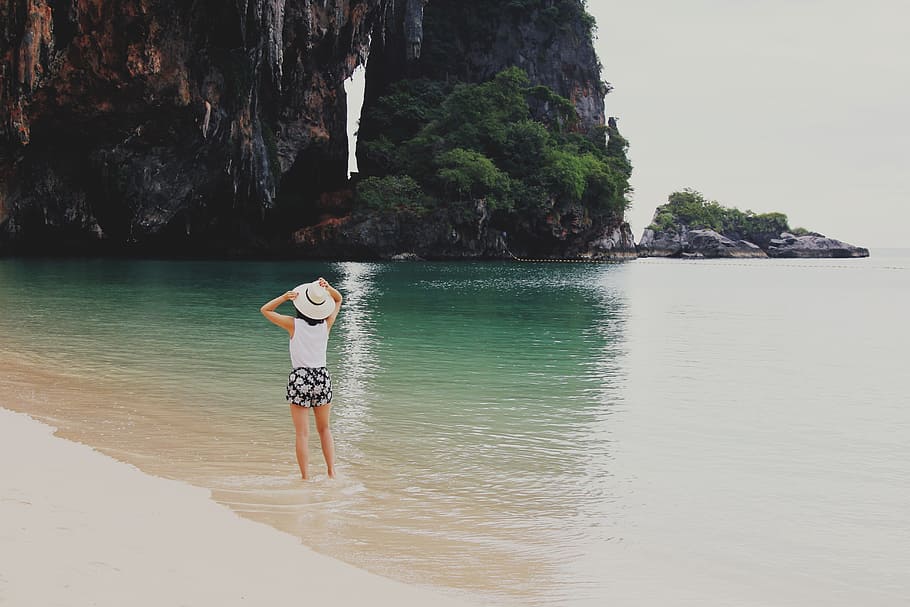 woman on body of water beside mountain, woman standing on seashore near cave HD wallpaper