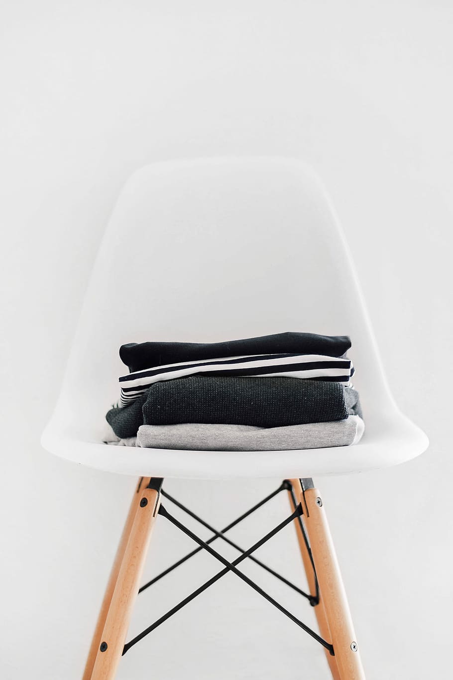 pile of black, white, and gray textiles on white padded chair with brown frame, folded clothes on white chair HD wallpaper