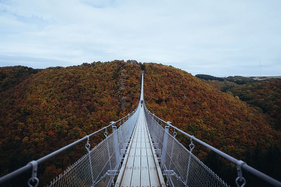 person walking on white hanging bridge during daytime, gray hanging bridge through mountain
