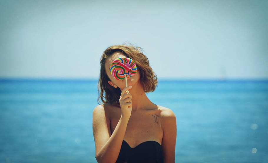 woman in black strapless top holding lollipop, sea, ocean, candy