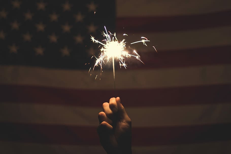 person holding sparkler, person holding lighted sparkler in front of U.S.A. flag HD wallpaper