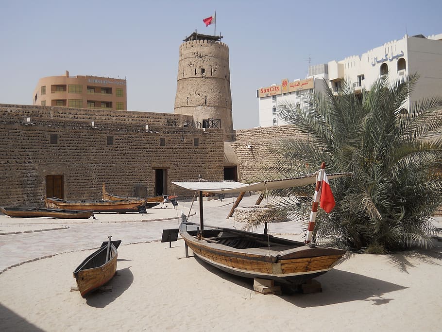 two brown wooden boats on white sand surrounded by grey brick wall and watch tower at daytime HD wallpaper