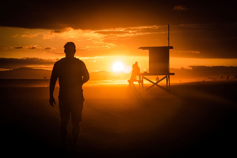 silhouette of man standing near wooden shed during sunset, man's silhouette standing near brown house