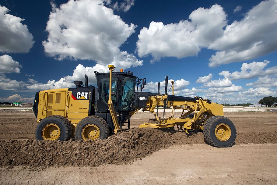 yellow CAT grader on plane dirt field during daytime, mining vehicle