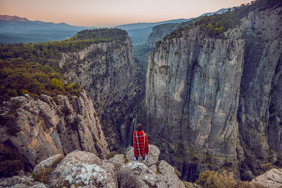 person standing on peak front of rock formation at daytime, person wearing red and black plaid top standing on cliff HD wallpaper