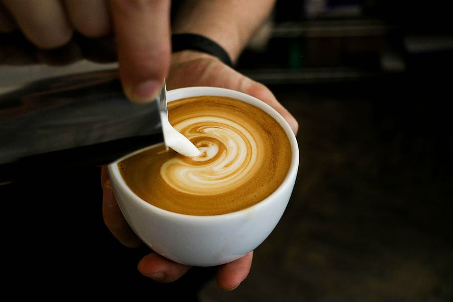 person pouring latte in coffee making art, adding, milk, cup